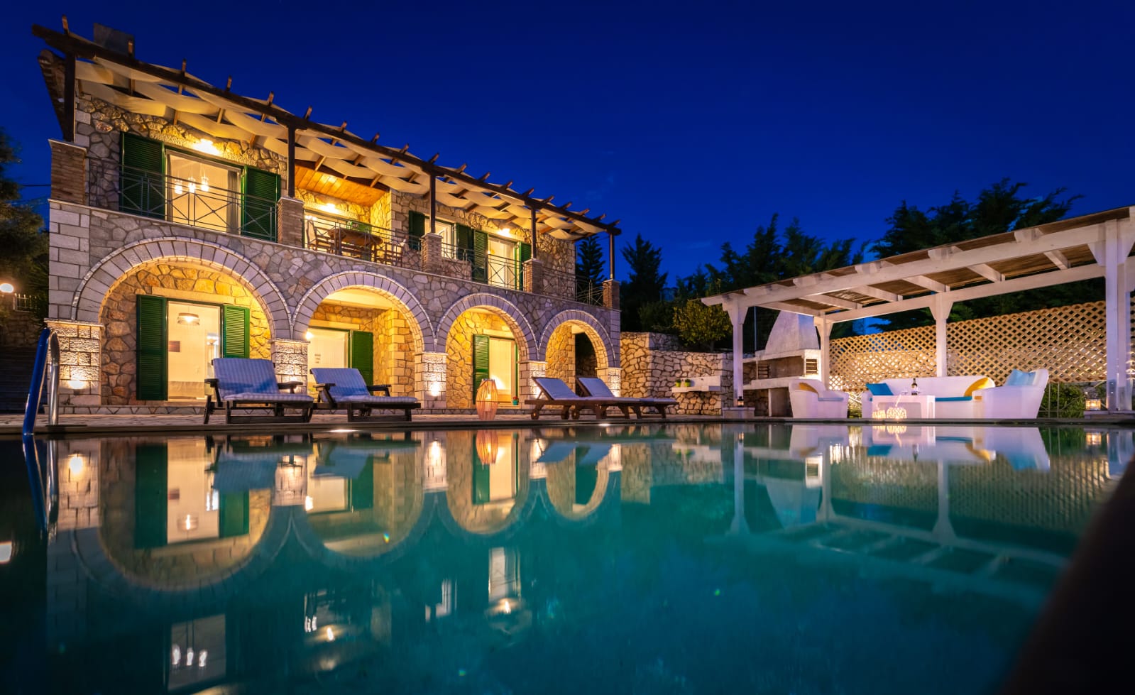 Villa Emma lit up at twilight, mirrored in the pool